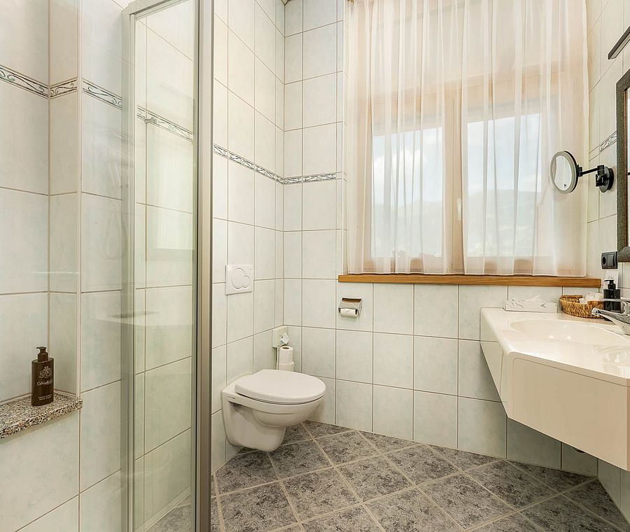 Modern bathroom with shower, toilet, mirror and window with curtains in hotel room