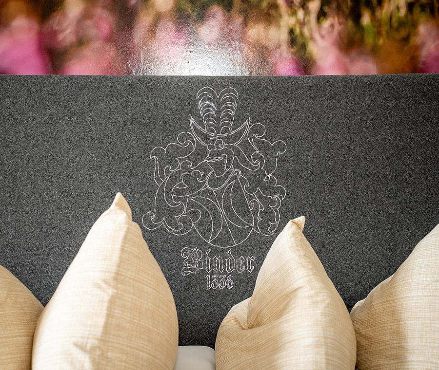 Headboard with embroidered crest and two beige pillows in a cozy hotel room