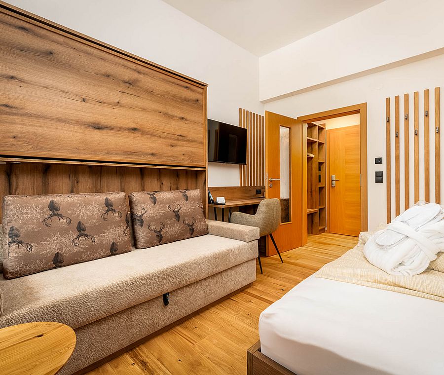 Living area with sofa, wooden details, TV and desk in hotel room