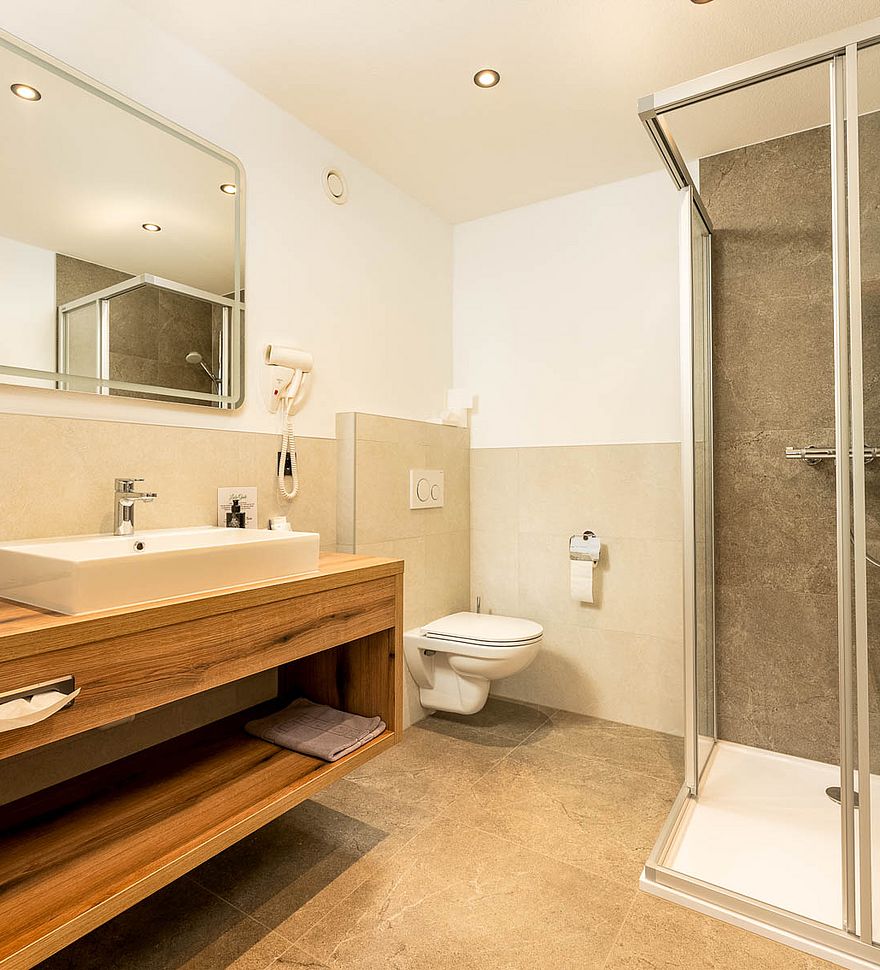 Modernes Bad mit großer Dusche, Holzwaschtisch, Spiegel, Toilette und hellen Fliesen