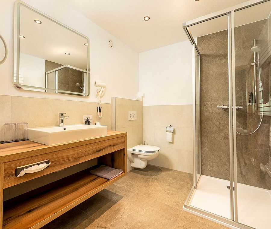 Modern bathroom with large shower, wooden washstand, mirror, toilet and bright tiles