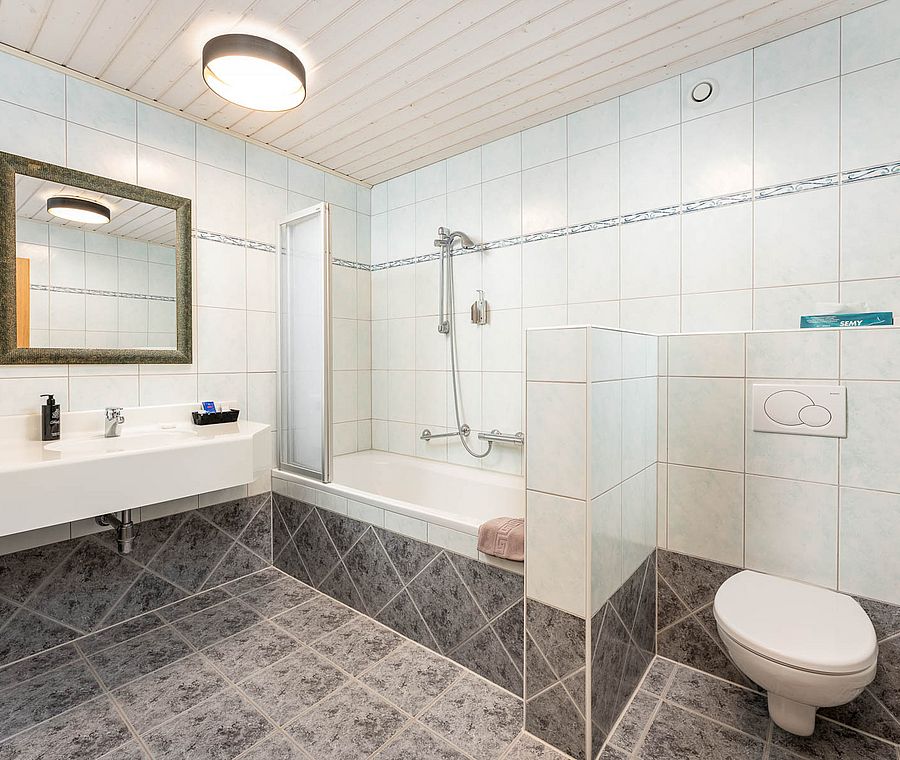 Modern bathroom with tiles, bathtub, shower, mirror and toilet in a hotel room