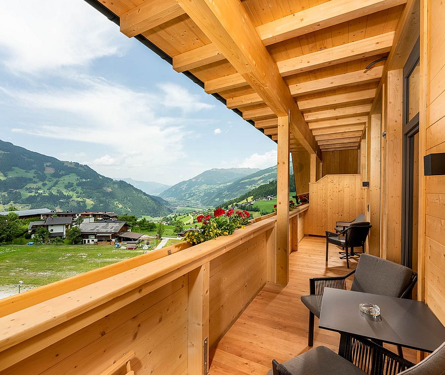 Covered wooden balcony with seating, flower boxes and panoramic view of valley and mountains