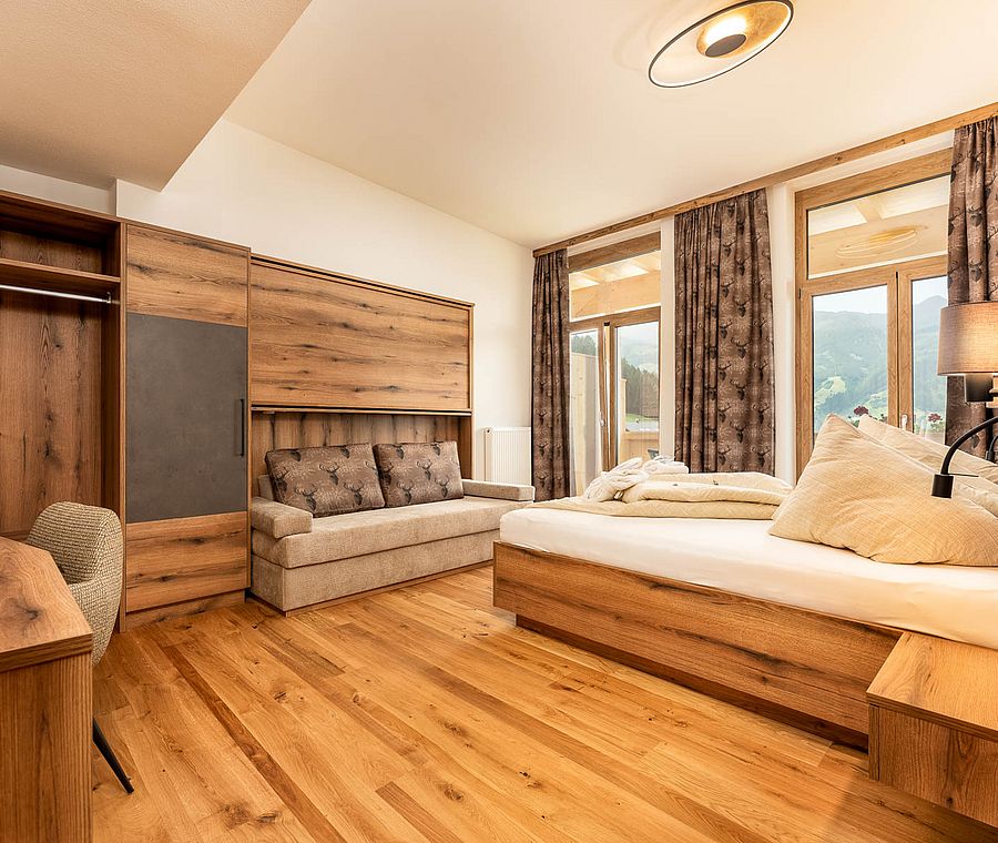 Spacious room with double bed, sofa, lots of wood, open wardrobe and balcony with mountain view