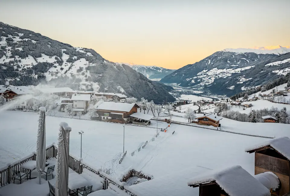 Panorama über das verschneite Zillertal mit orangefarbenem Abendhimmel und Hütten