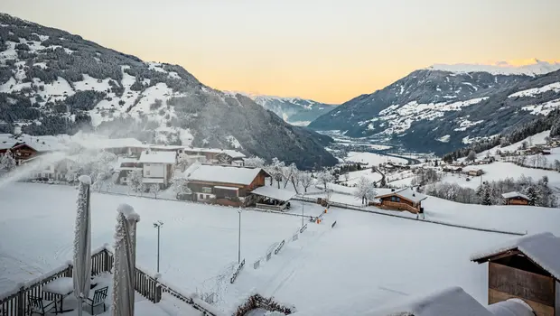 Panorama über das verschneite Zillertal mit orangefarbenem Abendhimmel und Hütten