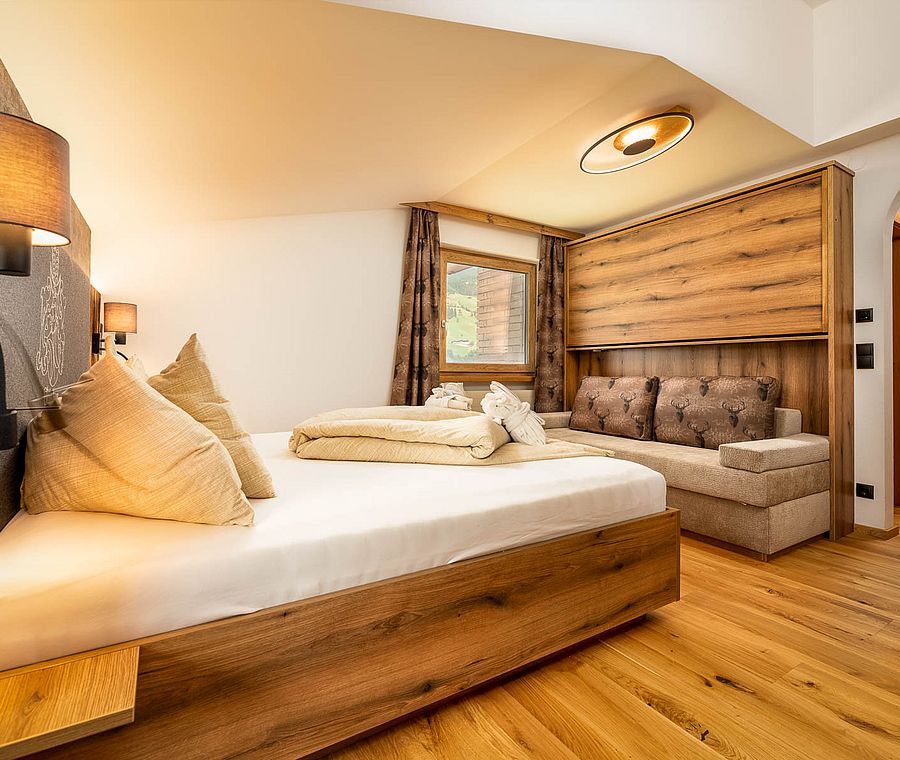 Hotel room with double bed, sofa, parquet flooring, wooden details and modern lamps